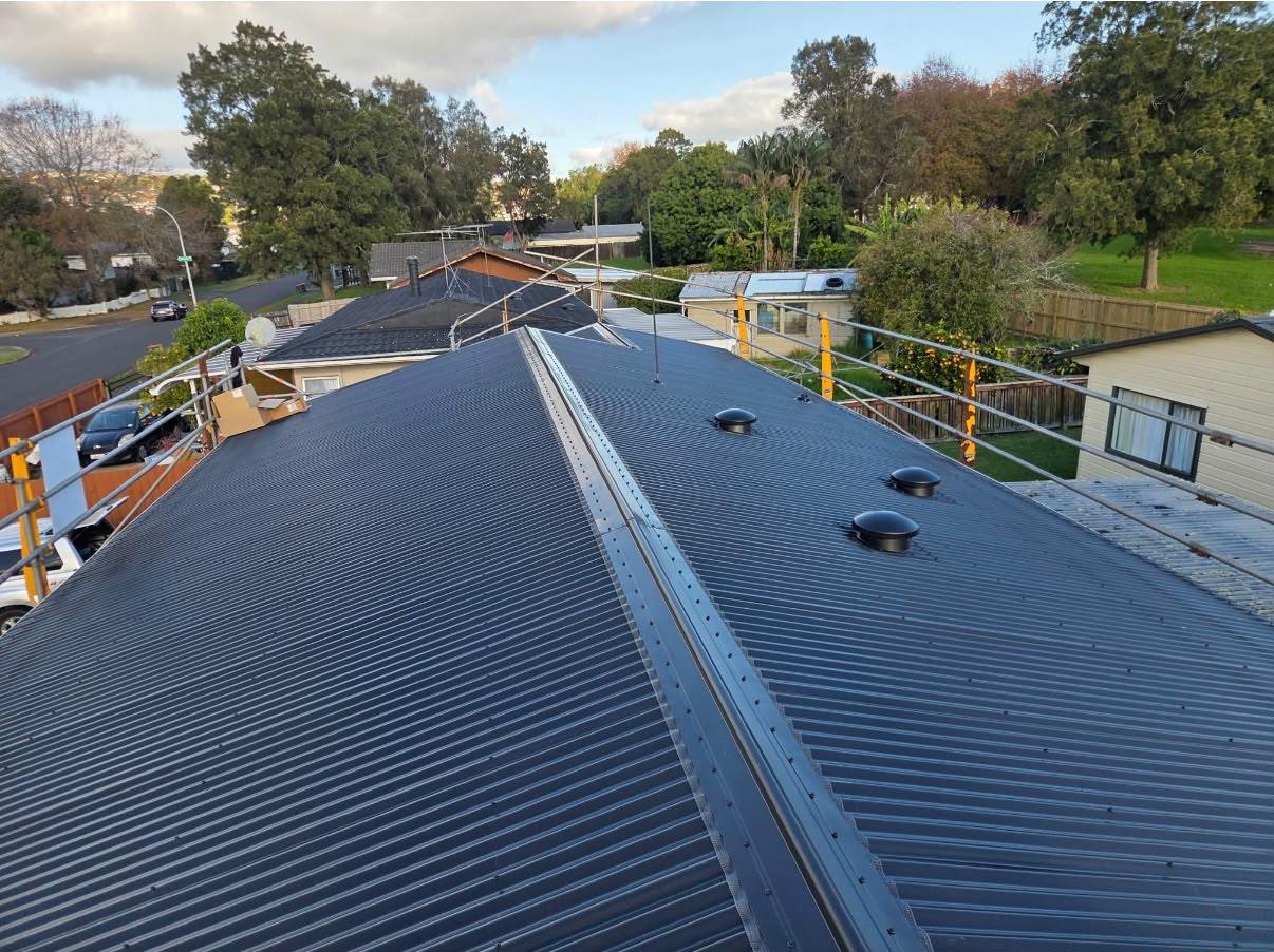 The finished dark long-run roof with edge protection rails still up along the eaves