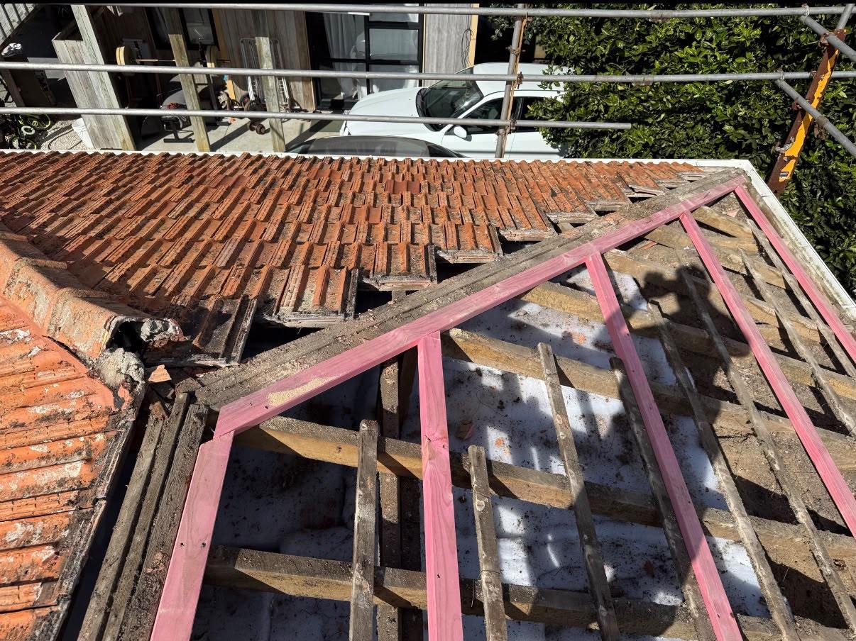 An old concrete tile roof part-stripped, with the original tiles still on one hip and new battens going down on the other